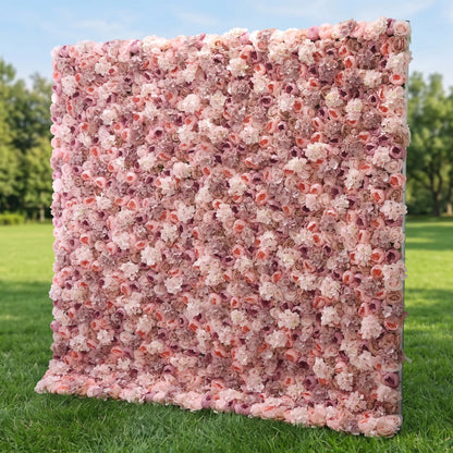 Lush full-panel blush artificial flower wall densely packed with layered dusty pink, peach, mauve and cream roses mixed with delicate filler blooms, displayed outdoors on a vibrant green lawn. This reusable, maintenance-free floral backdrop delivers soft romantic texture, ideal for wedding photo booths, bridal showers, boutique retail displays and pastel-themed social media content shoots for elegant, eye-catching event styling.