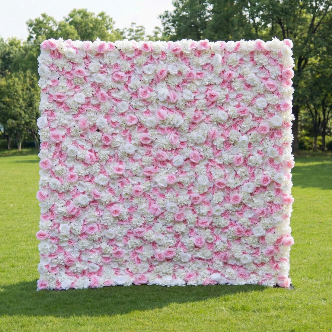 This outdoor floral backdrop (set on lush green grass, tree-framed) is a dense wall of soft pink roses and white filler blooms, creating an airy, romantic texture. The delicate, blush-and-ivory palette exudes gentle elegance, making it ideal for garden weddings, baby showers, or intimate outdoor events that lean into timeless, feminine charm.