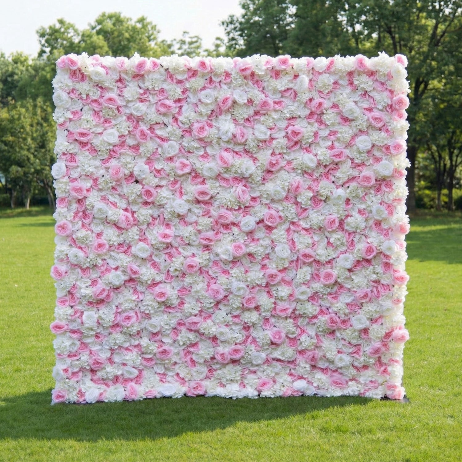 This outdoor floral backdrop (set on lush green grass, tree-framed) is a dense wall of soft pink roses and white filler blooms, creating an airy, romantic texture. The delicate, blush-and-ivory palette exudes gentle elegance, making it ideal for garden weddings, baby showers, or intimate outdoor events that lean into timeless, feminine charm.