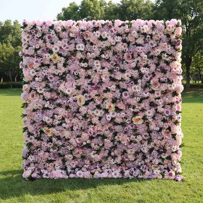 Romantic full-size artificial flower wall densely layered with blush roses, lavender hydrangeas, white daisies and soft mauve filler blooms, set on a bright green outdoor lawn. This reusable, zero-maintenance floral backdrop offers rich layered pastel texture, perfect for wedding photo booths, bridal showers, baby parties and pastel-toned social media content shoots for gentle, eye-catching celebration decor.