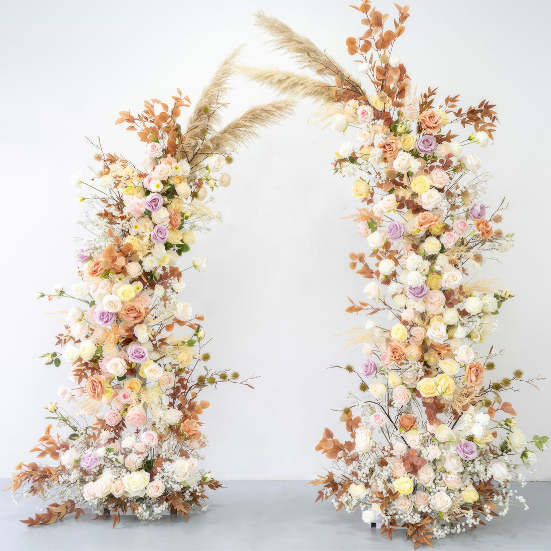 This is a beautifully crafted floral arch made of artificial flowers. It combines soft pastel tones like pink, lavender, and cream with warm earthy hues from the brownish - orange leaves and pampas grass. The arch exudes a romantic, natural, and bohemian style, perfect for weddings or garden - themed events. 