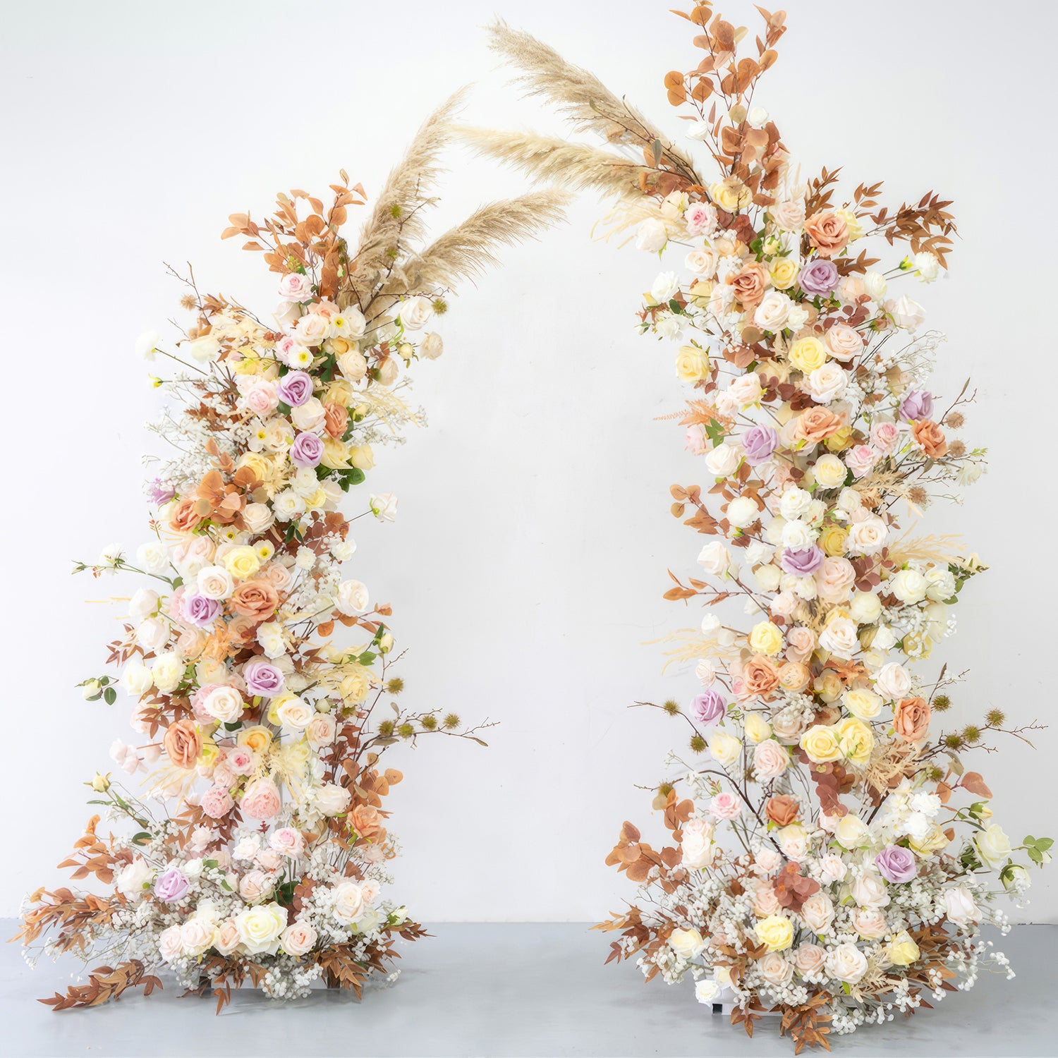 This is a beautifully crafted floral arch made of artificial flowers. It combines soft pastel tones like pink, lavender, and cream with warm earthy hues from the brownish - orange leaves and pampas grass. The arch exudes a romantic, natural, and bohemian style, perfect for weddings or garden - themed events. 