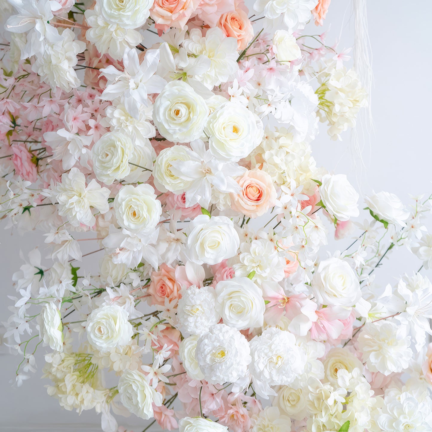 This image showcases an arrangement of artificial flowers in soft hues of white, light pink, and peach. It includes roses and chrysanthemums. The style is gentle and romantic, evoking a sense of elegance. 