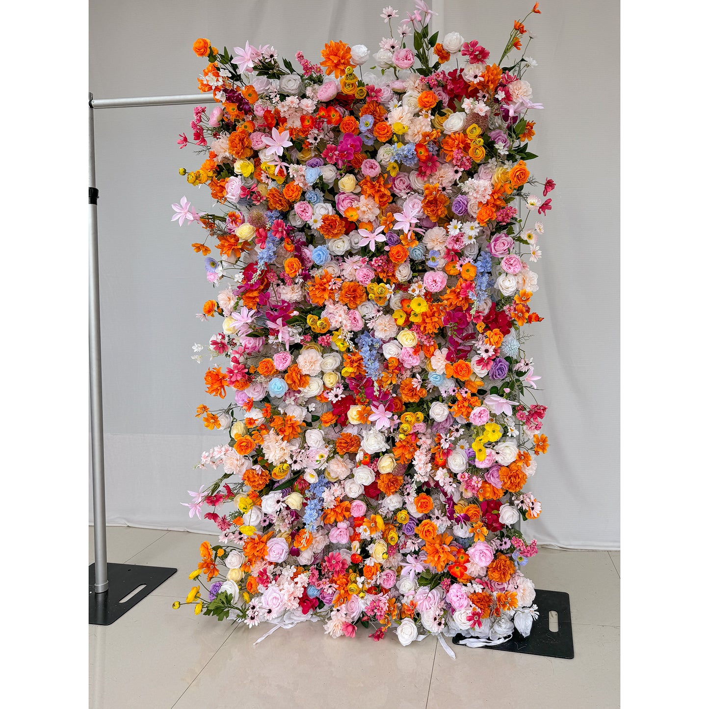 This image showcases a 1.2x2.4m(4*8ft) vibrant floral wall adorned with a rich variety of artificial flowers. The colors are a vivid mix of bright orange, soft pink, deep red, delicate blue, creamy white, and sunny yellow. Flower types include roses, daisies, and other assorted blooms, creating a lively and cheerful style. The dense arrangement is eye - catching, perfect for events or photo backdrops. 