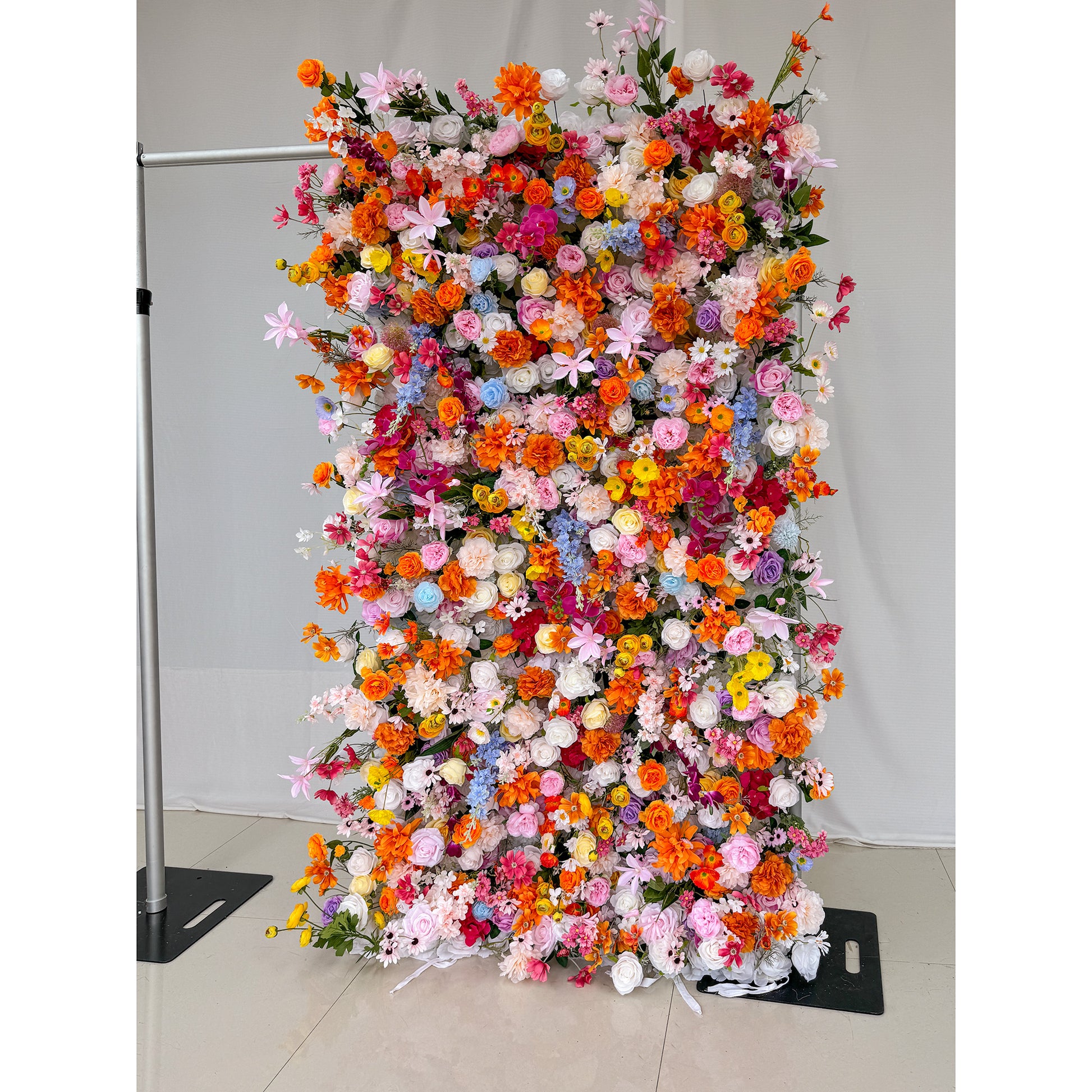 This image showcases a 1.2x2.4m(4*8ft) vibrant floral wall adorned with a rich variety of artificial flowers. The colors are a vivid mix of bright orange, soft pink, deep red, delicate blue, creamy white, and sunny yellow. Flower types include roses, daisies, and other assorted blooms, creating a lively and cheerful style. The dense arrangement is eye - catching, perfect for events or photo backdrops. 
