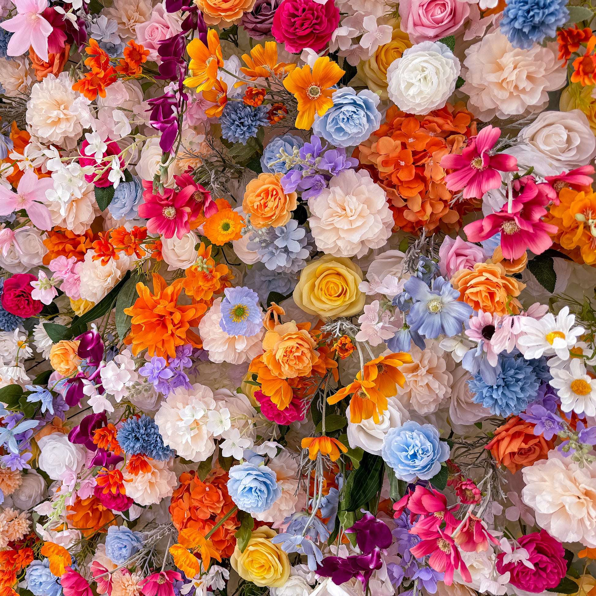 This image showcases a lush and vibrant floral arrangement featuring a variety of artificial flowers. Colors span a vivid spectrum, including bright orange, soft pink, deep purple, delicate blue, and creamy white. The flowers include roses, daisies, and other assorted blooms, creating a lively and whimsical style. The dense arrangement exudes a cheerful and celebratory atmosphere. 