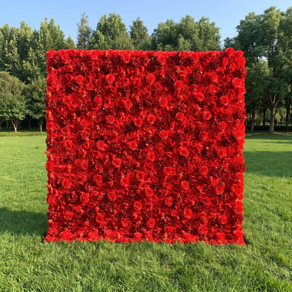 Stunning solid bright red artificial rose flower wall with dense full bloom coverage, placed on a sunlit green lawn backed by lush tall trees. This reusable, weatherproof floral backdrop delivers bold romantic drama, perfect for wedding photo booths, Valentine’s events, anniversary parties, boutique retail displays and vivid red-themed social media content shoots for eye-catching statement event decor.