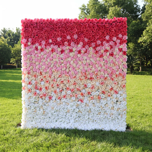 Gradient ombre artificial rose flower wall with seamless vertical color shift from deep crimson red at the top, soft blush pink midsection to clean creamy white at the bottom, set on a sunlit green lawn with leafy trees. This reusable, low-maintenance floral backdrop features dense full blooms, ideal for wedding photo booths, bridal showers, romantic brand shoots and pastel-red themed event decor for eye-catching layered gradient styling.