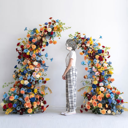 The image shows a person standing before a floral arch. Colors are a vibrant mix of blue, orange, red, yellow and pastel hues. Styles include roses and daisies. The overall look is lively and celebratory. 