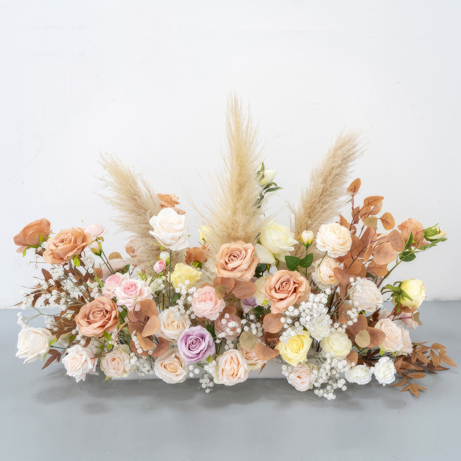 This is a charming artificial flower arrangement. It features roses in soft pastel colors such as peach, pink, lavender, and cream. Accented with pampas grass and brownish - orange leaves, along with small white filler flowers, it has a warm, natural, and romantic style. 
