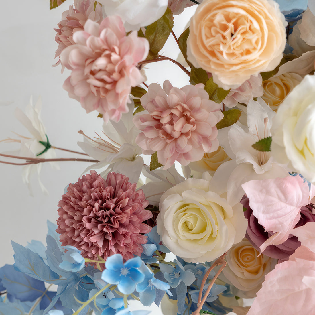 This floral arrangement features a charming mix of colors including soft pinks, creamy whites, warm peaches, and cool blues. With roses, dahlias and other blooms, it offers a sweet, delicate style, perfect for adding a touch of beauty to events like weddings or home decor.