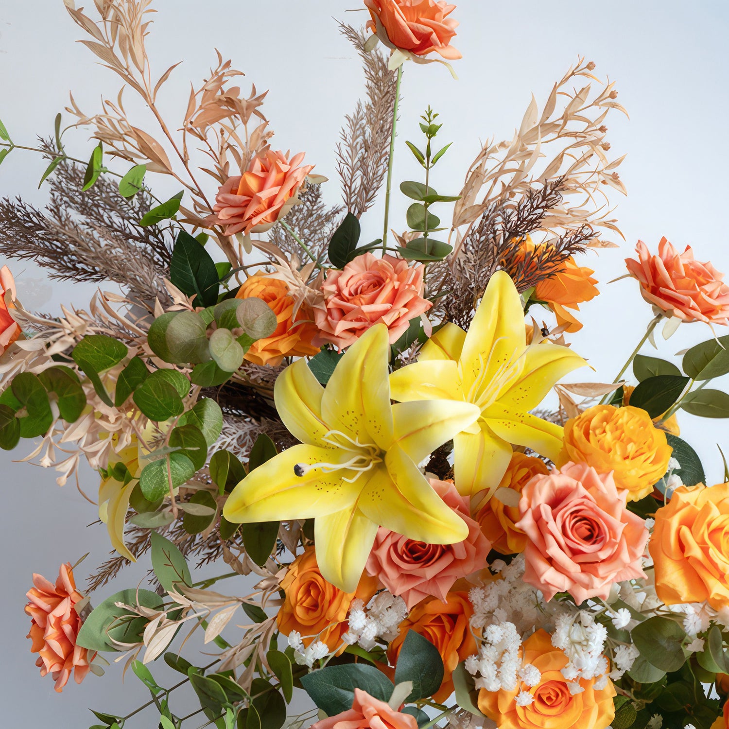 This is a colorful flower arrangement. It prominently features bright yellow lilies, surrounded by various shades of orange roses. Interspersed are some white baby&