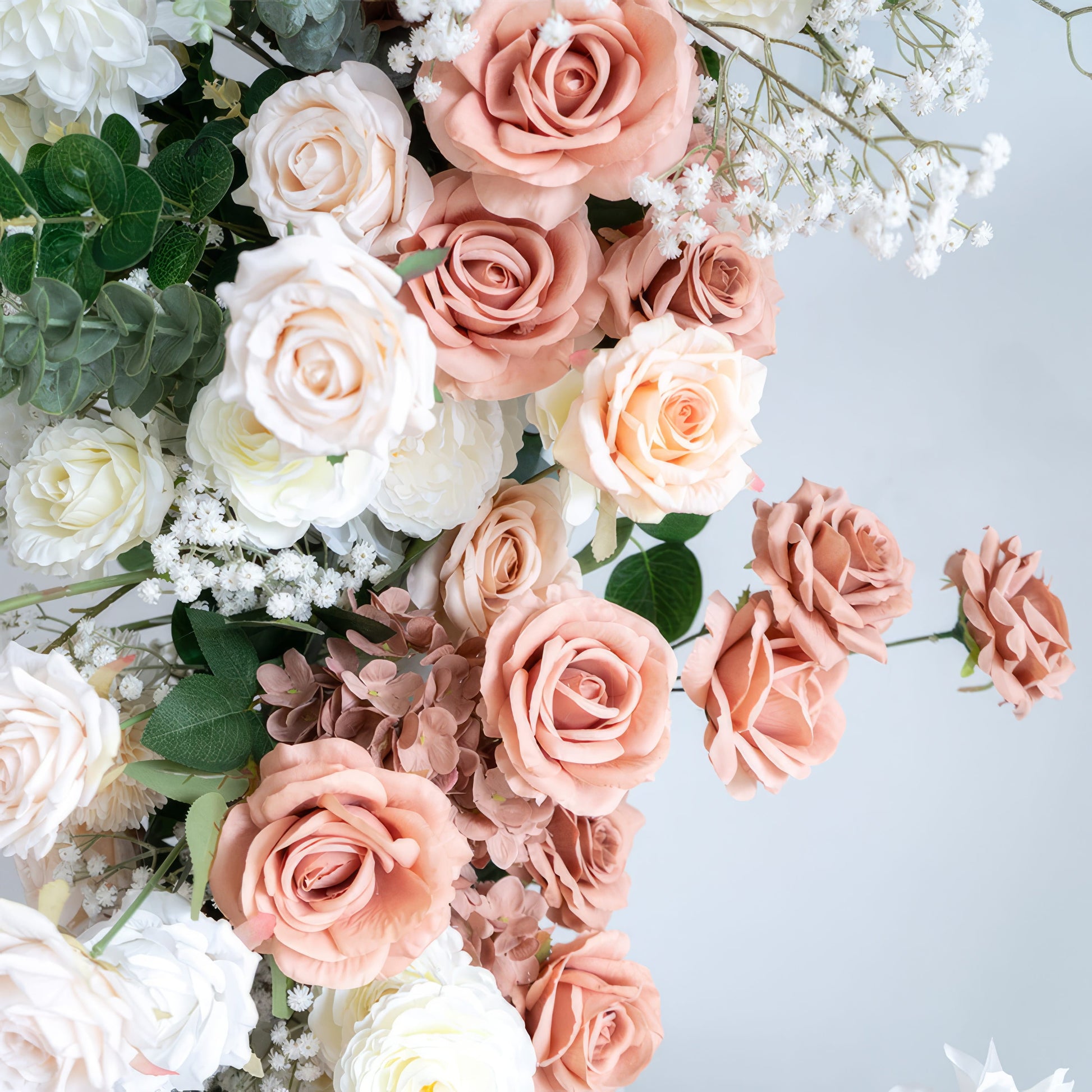 A close-up of a lush floral arrangement from Valar Flowers, featuring a harmonious blend of blush pink, terracotta, creamy white, and ivory roses, interspersed with delicate baby's breath and silvery-green eucalyptus. The soft, layered petals and fresh greenery create a romantic, elegant aesthetic, ideal for wedding decor, centerpieces, or special event accents.