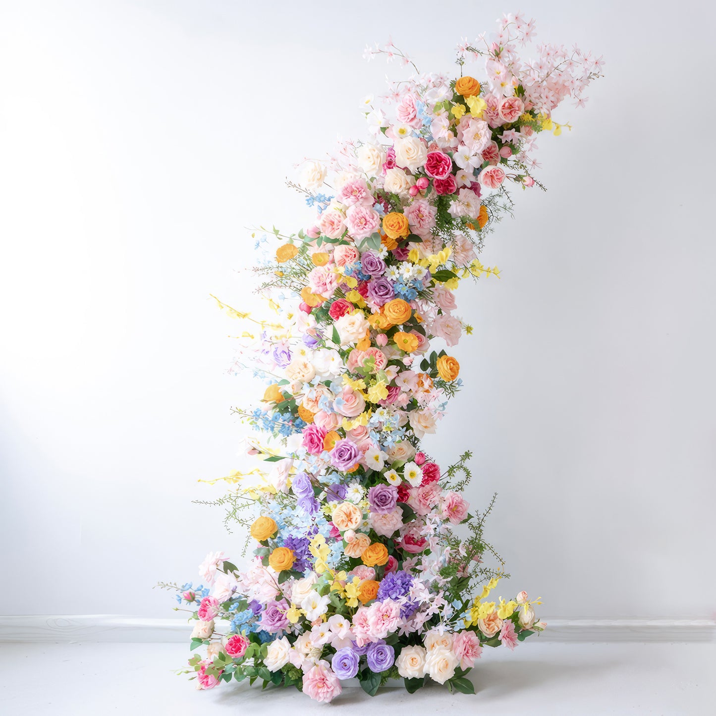 This is a strikingly beautiful floral arch adorned with a rich array of artificial flowers. It showcases a vivid color palette, including soft pinks, purples, yellows, oranges, and whites. Roses, hydrangeas, and small daisy - like flowers blend together. The overall style is exuberant and celebratory, perfect for weddings or festive gatherings. 