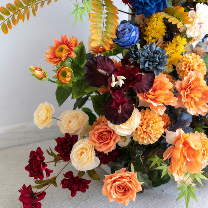 This image displays a colorful artificial flower arrangement. Colors range from deep red and blue to soft cream and bright orange. It includes roses and dahlias. The style is rich and vibrant, exuding a festive atmosphere. 