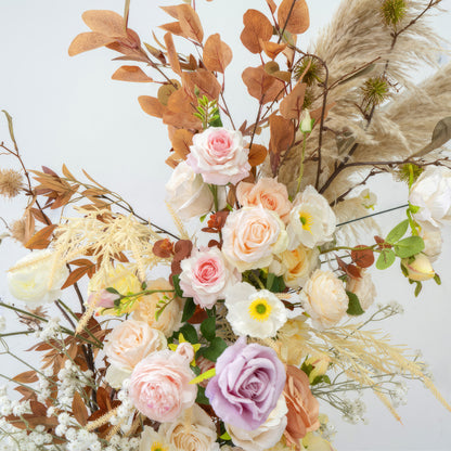 This artificial flower arrangement features a harmonious blend of pastel - colored roses in shades of pink, peach, and lavender. It also includes white daisy - like flowers, along with brownish - orange leaves and pampas grass. The overall style is warm, natural, and exudes a romantic charm. 