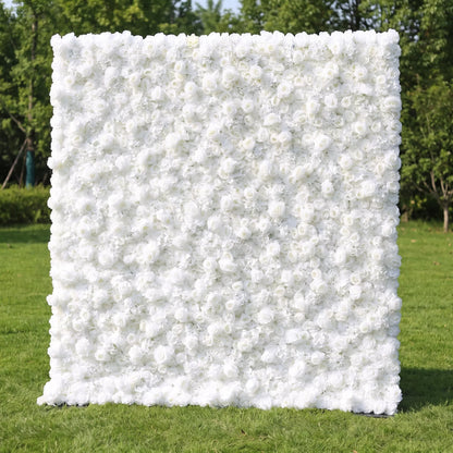 Full dense all-white artificial flower wall covered in layered white roses and delicate airy filler blooms, set on a sunlit green lawn with leafy trees in the background. This reusable, zero-maintenance floral backdrop delivers sleek minimalist luxury, ideal for wedding photo booths, baptism ceremonies, brand boutique displays and neutral clean aesthetic social media content shoots for timeless bright elegant event decor.