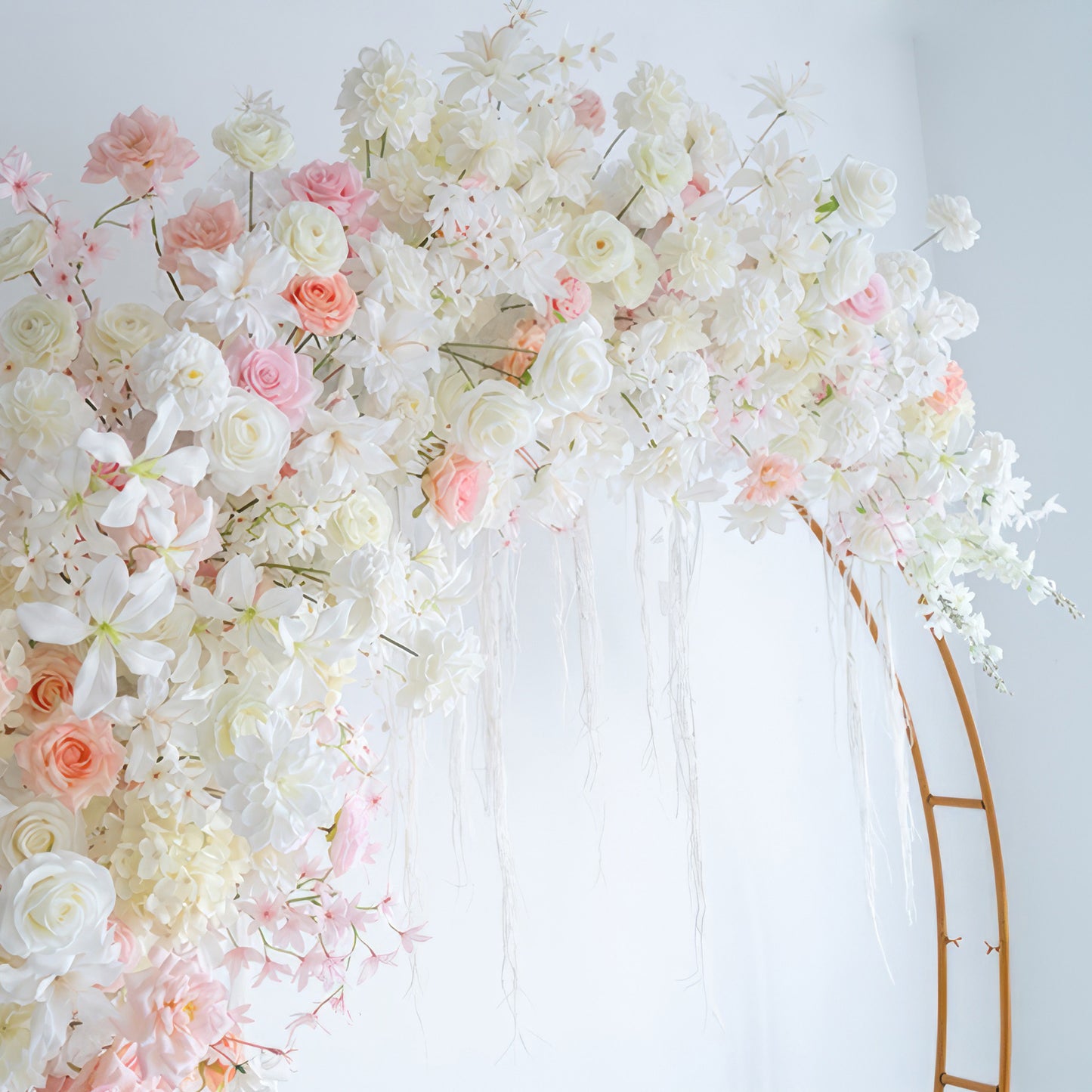 This image shows an artificial floral arrangement on a circular frame. It features roses, hydrangeas, and other blooms in soft colors of white, light pink, and peach. The style is romantic and ethereal. 
