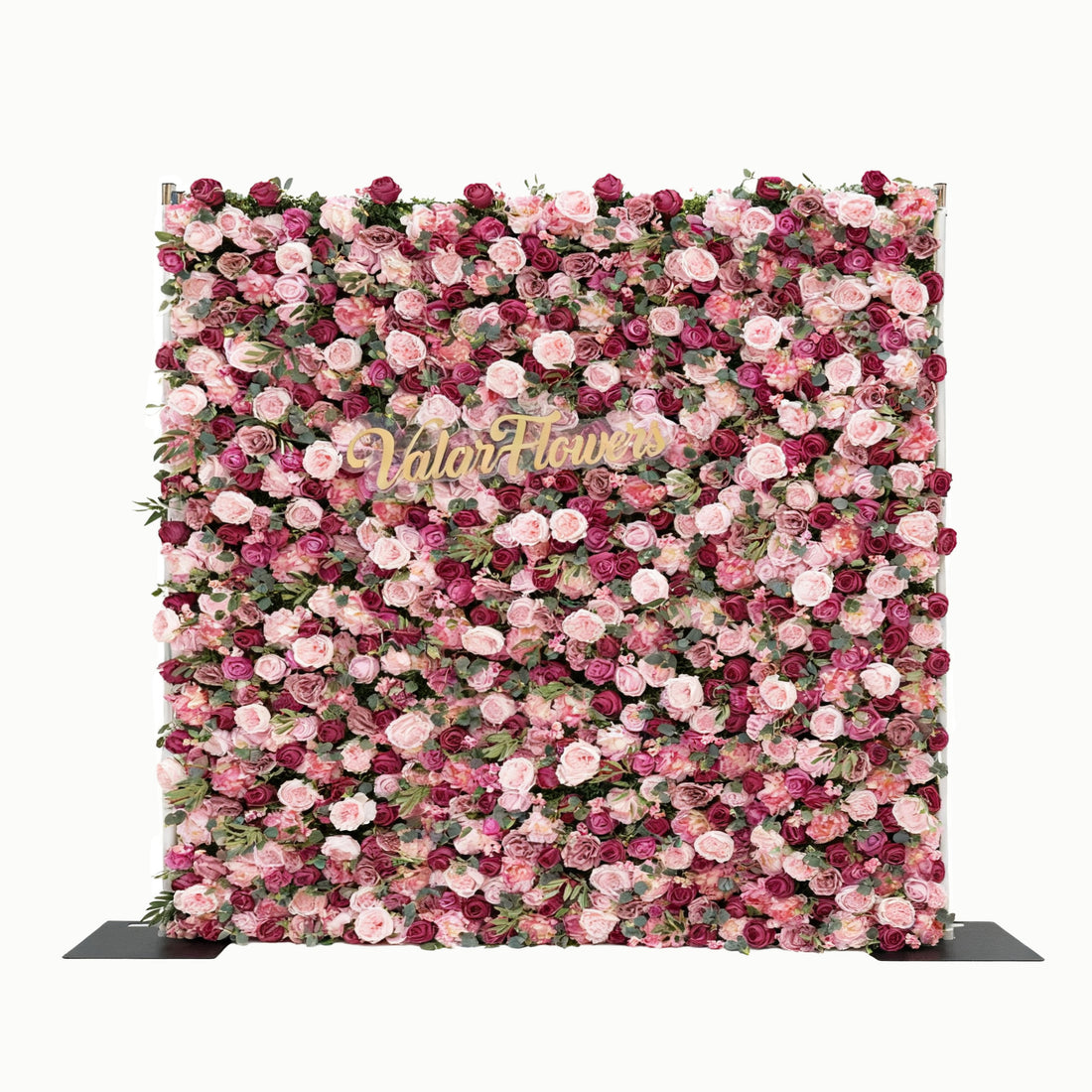 This image features a large, square floral wall composed of roses in various shades of pink and purple. In the center, golden text reads "Valar Flowers". The dense arrangement of flowers creates a lush and elegant look, making it suitable for decorative purposes, such as events or photo backdrops, exuding a romantic and sophisticated atmosphere.