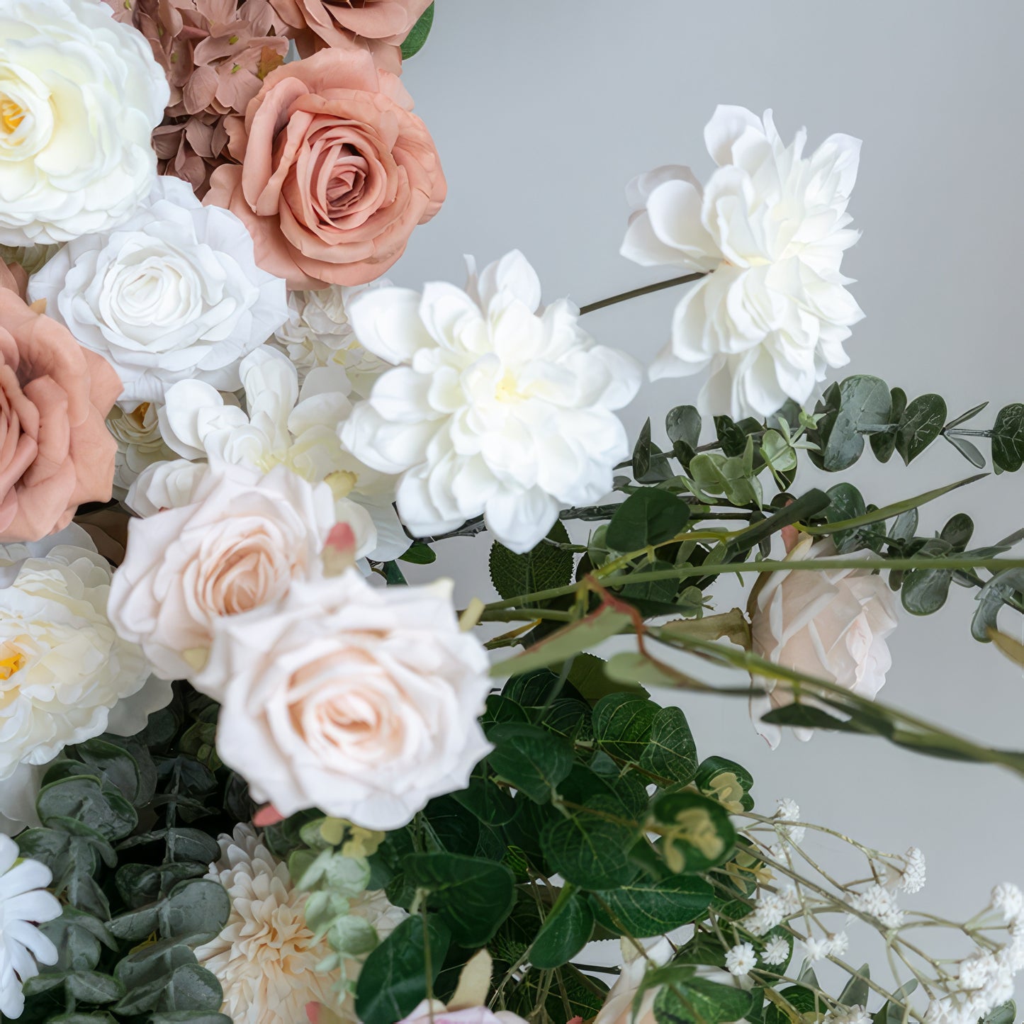 A close-up of a lush floral arrangement from Valar Flowers, featuring a harmonious blend of blush pink, terracotta, creamy white, and ivory roses, paired with voluminous white dahlias and delicate baby's breath, all intertwined with silvery-green eucalyptus. The soft, layered petals and fresh greenery create a romantic, elegant aesthetic, ideal for wedding decor, centerpieces, or special event accents.
