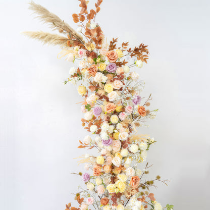 This is a vertical artificial flower arrangement. It features roses in pastel colors like peach, pink, lavender and cream, along with brownish - orange leaves and pampas grass. The style is warm, natural and bohemian. 