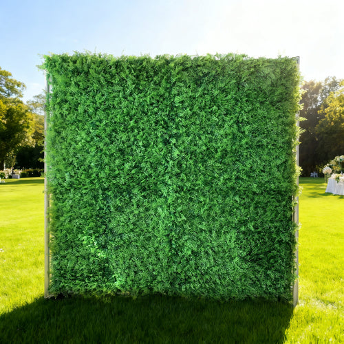 This image showcases a lush artificial greenery backdrop by ValarFlowers, set outdoors on a vibrant lawn. It features dense, uniform green foliage, creating a rich, natural, and visually refreshing display. Bathed in sunlight, with a scenic park and event setup in the background, this piece is perfect for adding organic elegance to outdoor events, exuding a serene and sophisticated atmosphere.