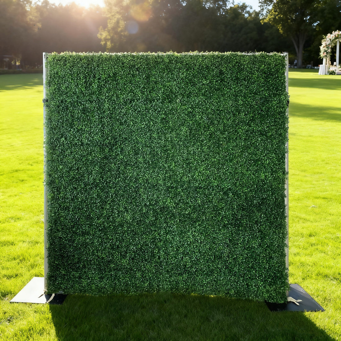 This image showcases a lush artificial greenery wall by ValarFlowers, set outdoors on a vibrant lawn. It features dense, uniform green foliage, creating a rich, natural, and visually refreshing display. Bathed in sunlight, this piece is perfect for adding organic elegance to events or spaces, exuding a serene and sophisticated atmosphere.