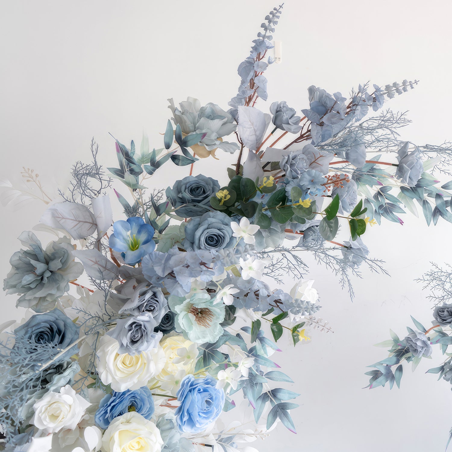 This image features an artificial flower arrangement with a cool and calming color scheme of various blues and whites. It includes blue roses, white roses, and other blue - toned blooms, complemented by different types of foliage. The overall style is elegant, serene, and gives a sense of tranquility. 