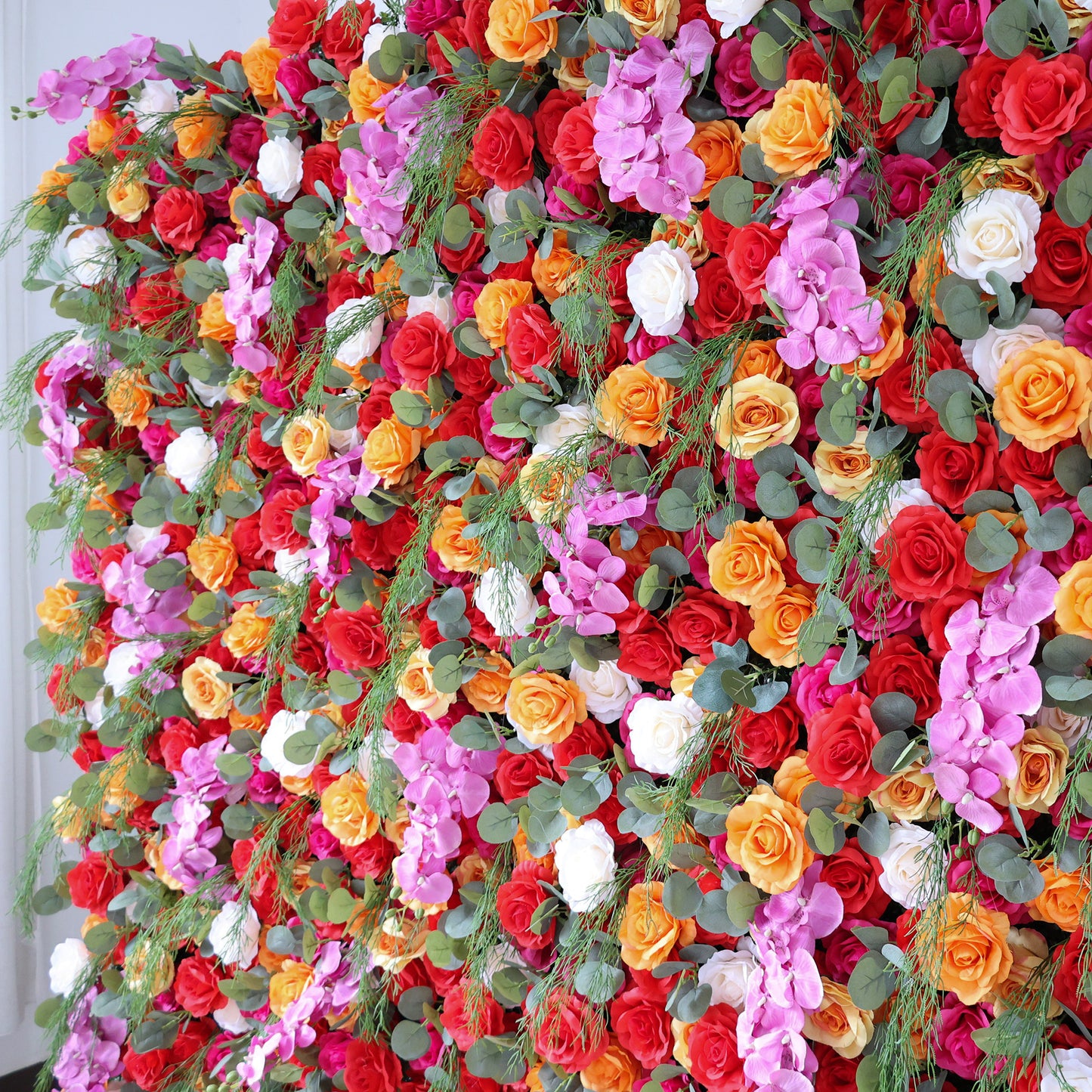 This image showcases a vibrant floral arrangement by Valar Flowers. It features a dense cluster of artificial flowers in a rich palette of red, orange, pink, and white, interspersed with lush green foliage. The blooms, including roses and other complementary flowers, are intricately arranged to create a lush, textured, and visually striking display. Perfect for adding a touch of energy and elegance to events or spaces, the arrangement exudes a lively and sophisticated atmosphere.