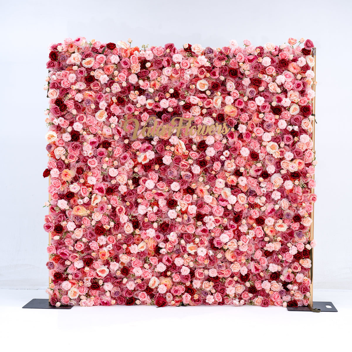A square floral wall backdrop covered in dense pink, red, and peach faux flowers, with a gold script logo reading 'Blush Florals' across the center, photographed against a clean white background.