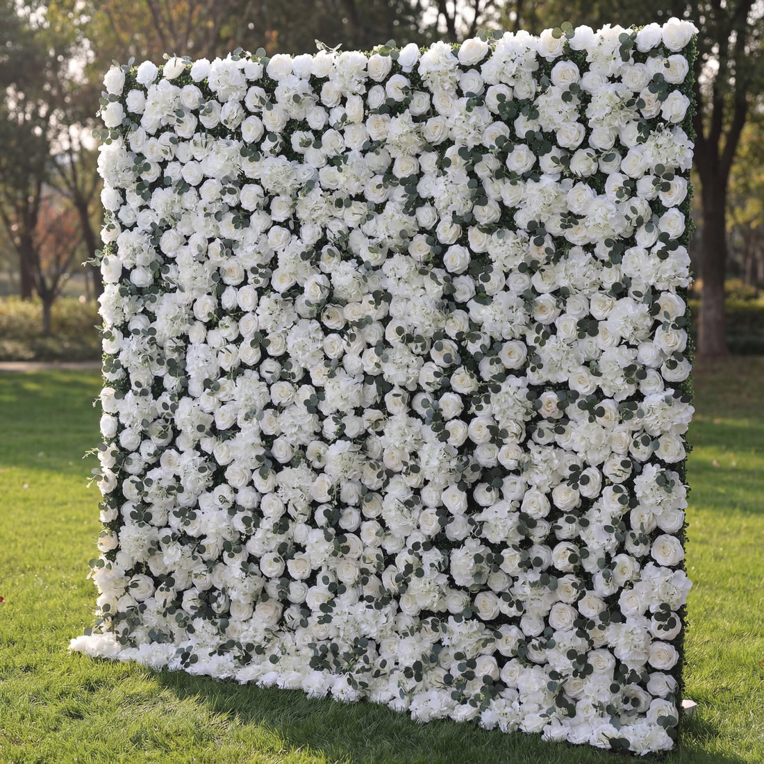 This elegant floral backdrop is densely covered in white blooms—including roses and hydrangeas—interspersed with tiny green foliage accents. The uniform, lush texture features soft petal variations and subtle white-to-cream gradients, enhanced by natural sunlight that highlights its fresh, opulent appearance. Its crisp, monochromatic display blends classic sophistication with organic fullness, making it a versatile focal point ideal for weddings, formal events, or minimalist outdoor decor.