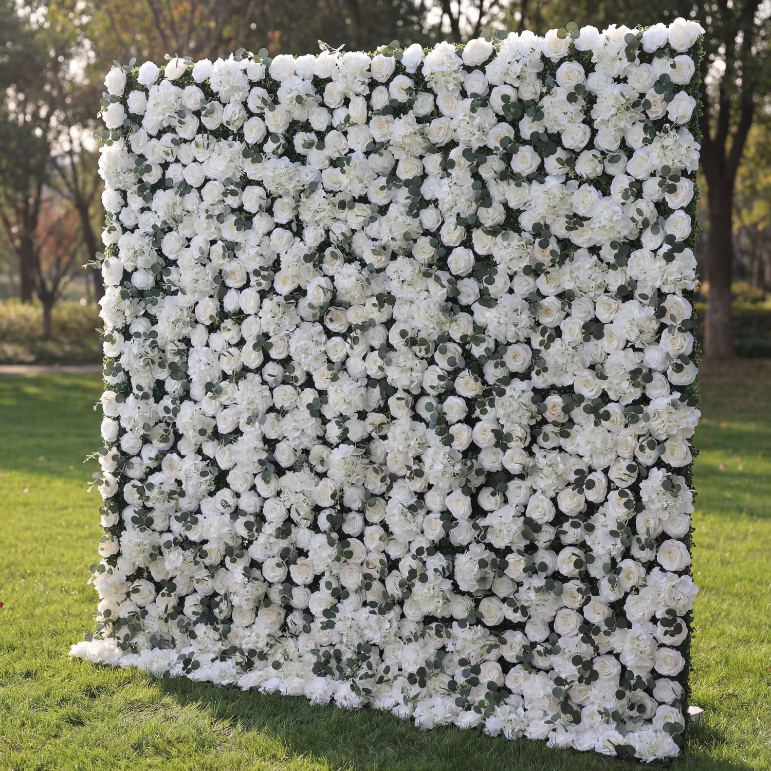 This elegant floral backdrop is densely covered in white blooms—including roses and hydrangeas—interspersed with tiny green foliage accents. The uniform, lush texture features soft petal variations and subtle white-to-cream gradients, enhanced by natural sunlight that highlights its fresh, opulent appearance. Its crisp, monochromatic display blends classic sophistication with organic fullness, making it a versatile focal point ideal for weddings, formal events, or minimalist outdoor decor.