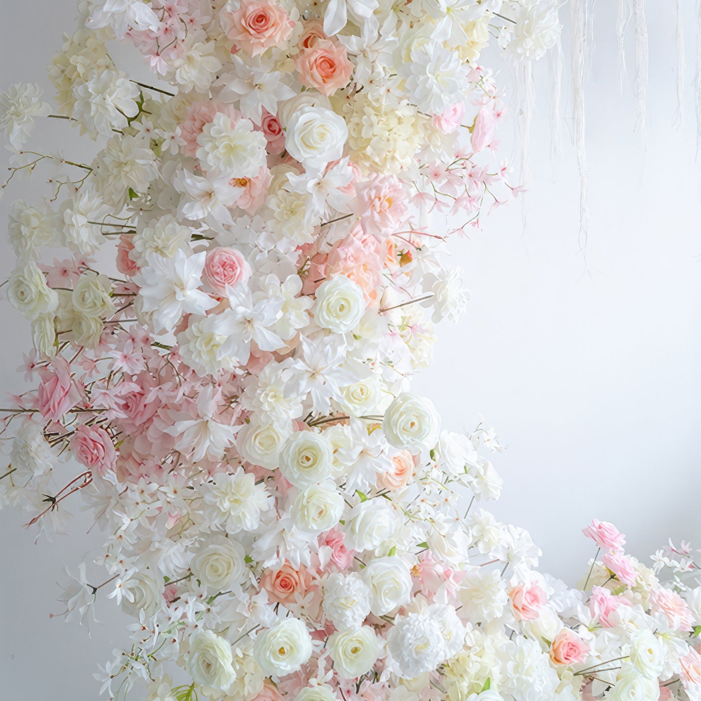 This image showcases an artificial flower display with roses, hydrangeas, and other blossoms in a palette of white, light pink, and peach. The style is soft and romantic, exuding an elegant charm. 