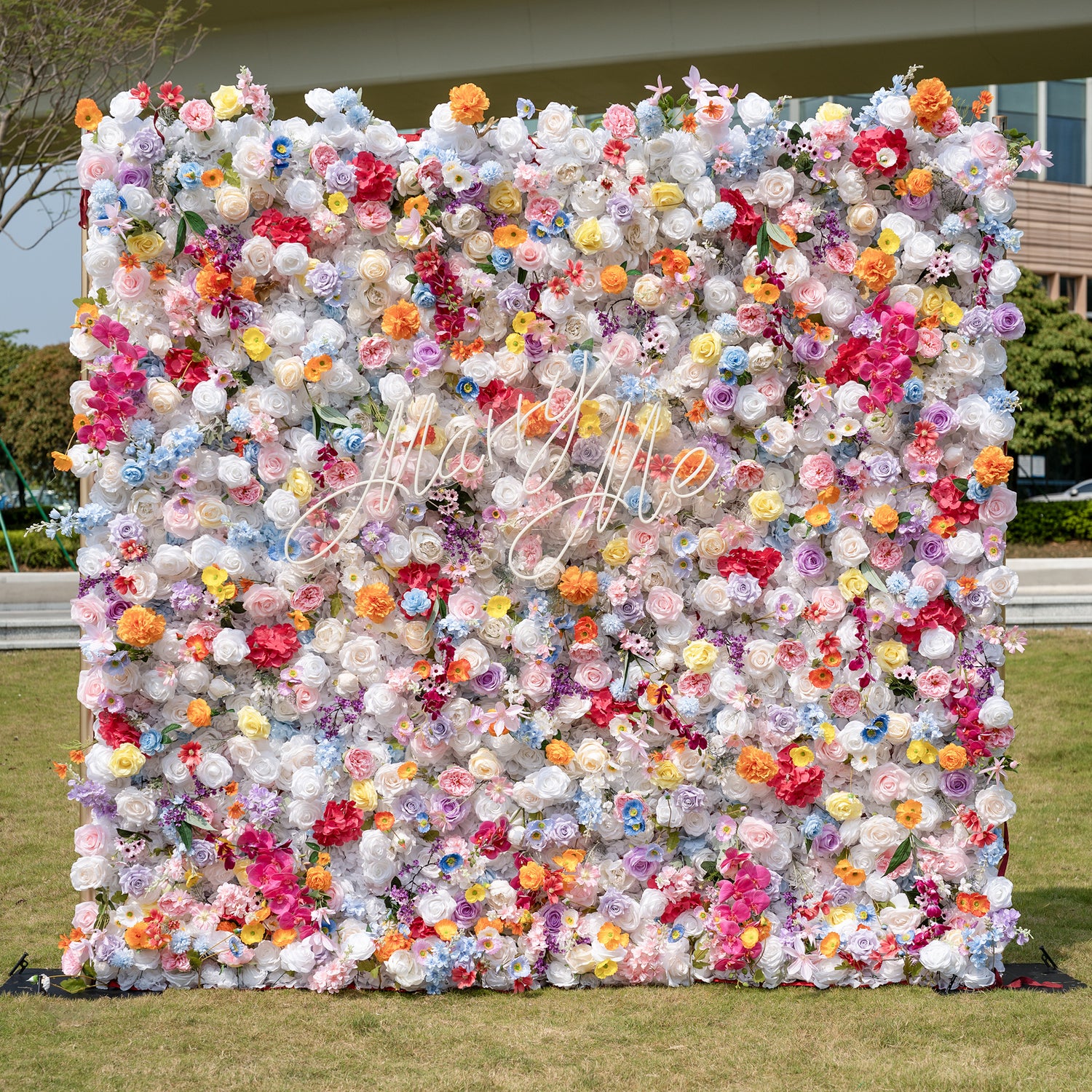 This is a stunning, dense artificial flower wall backdrop from Valar Flowers, brimming with a vibrant, rainbow-hued mix of lifelike blooms. It features creamy white roses, soft pink peonies, sunny yellow poppies, vivid orange carnations, sky-blue delphiniums, deep magenta orchids, and delicate filler flowers, creating a lush, romantic focal point perfect for outdoor weddings, proposals, engagement parties, photo booths, and luxury event decor.