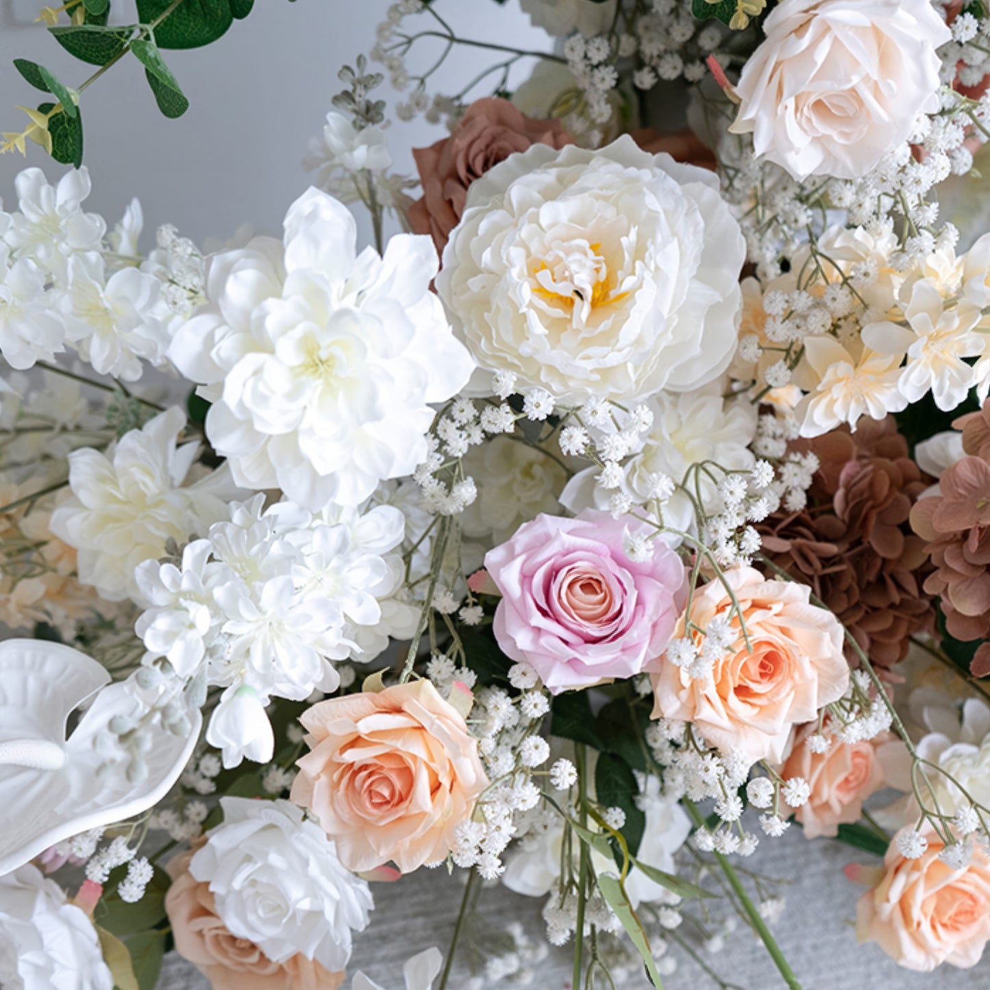 A close-up of a lush floral arrangement from Valar Flowers, featuring a harmonious blend of blush pink, terracotta, creamy white, and ivory blooms—including roses, peonies, and delicate baby's breath—intertwined with silvery-green eucalyptus and white anthuriums. The soft, layered petals and fresh greenery create a romantic, elegant aesthetic, ideal for wedding decor, centerpieces, or special event accents.