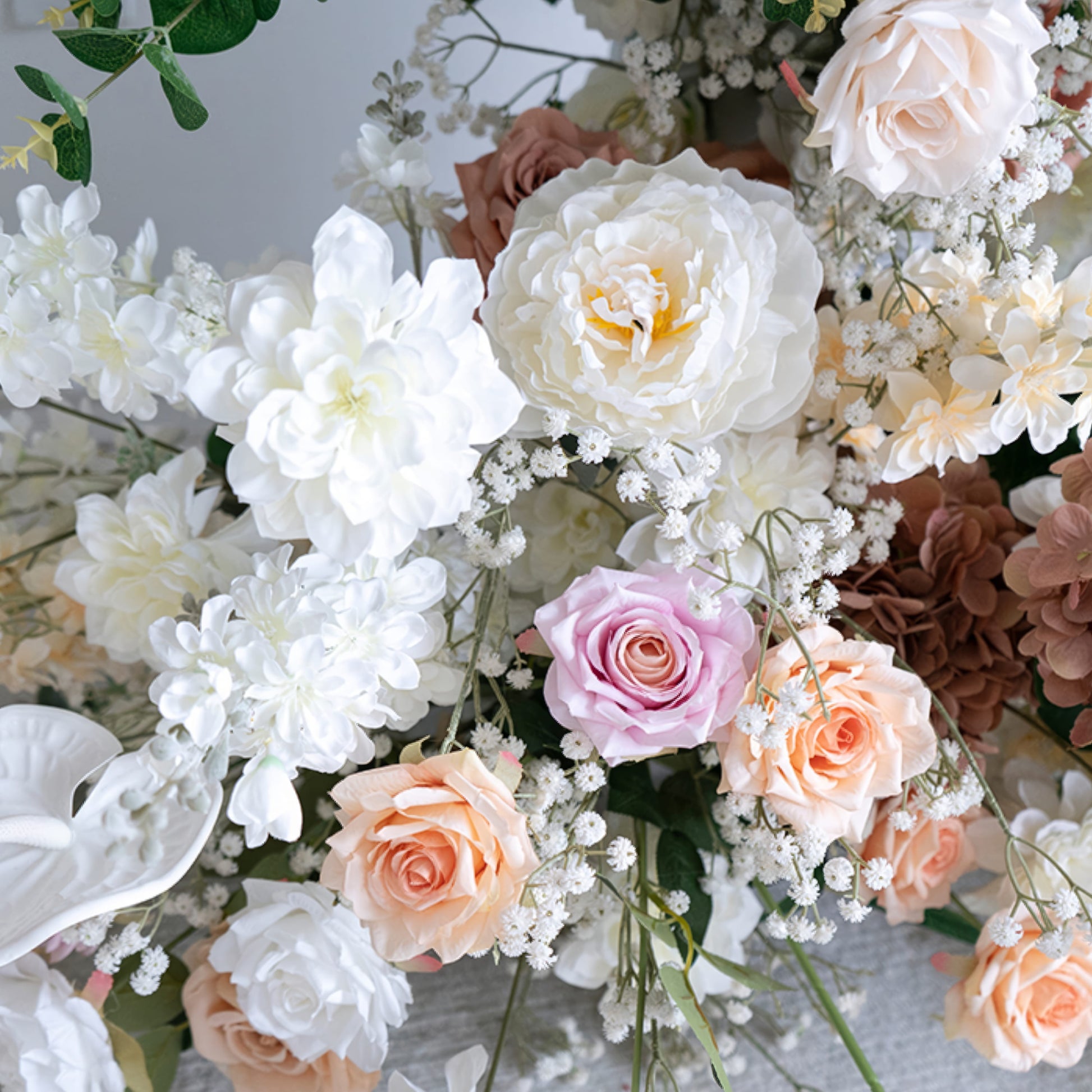 A close-up of a lush floral arrangement from Valar Flowers, featuring a harmonious blend of blush pink, terracotta, creamy white, and ivory blooms—including roses, peonies, and delicate baby's breath—intertwined with silvery-green eucalyptus and white anthuriums. The soft, layered petals and fresh greenery create a romantic, elegant aesthetic, ideal for wedding decor, centerpieces, or special event accents.