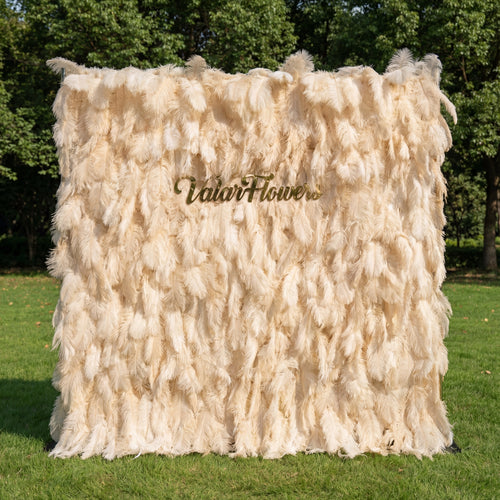 This opulent backdrop (set on sunlit grass, tree backdrop) is draped in lush, layered champagne-ivory artificial feathers, with soft gradients from pale cream to warm beige. A polished gold “ValarFlowers” sign anchors the center, glowing against the plush, airy plumage. Natural sunlight enhances the feathery texture’s depth, merging timeless neutral elegance with opulent metallic warmth to create a refined, sophisticated focal point—ideal for upscale outdoor events or romantic celebrations.