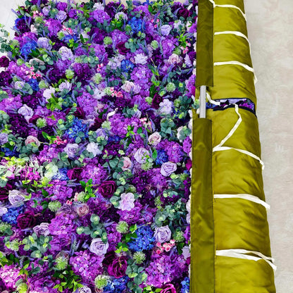 This image displays a vibrant floral arrangement dominated by various shades of purple, from deep violet to soft lavender, along with hints of blue and pink blooms. Interspersed with green foliage, the dense cluster creates a rich, lively, and elegant visual. Next to it is a rolled - up, olive - green fabric with white straps, possibly for storage or display purposes, adding a functional element to the scene.