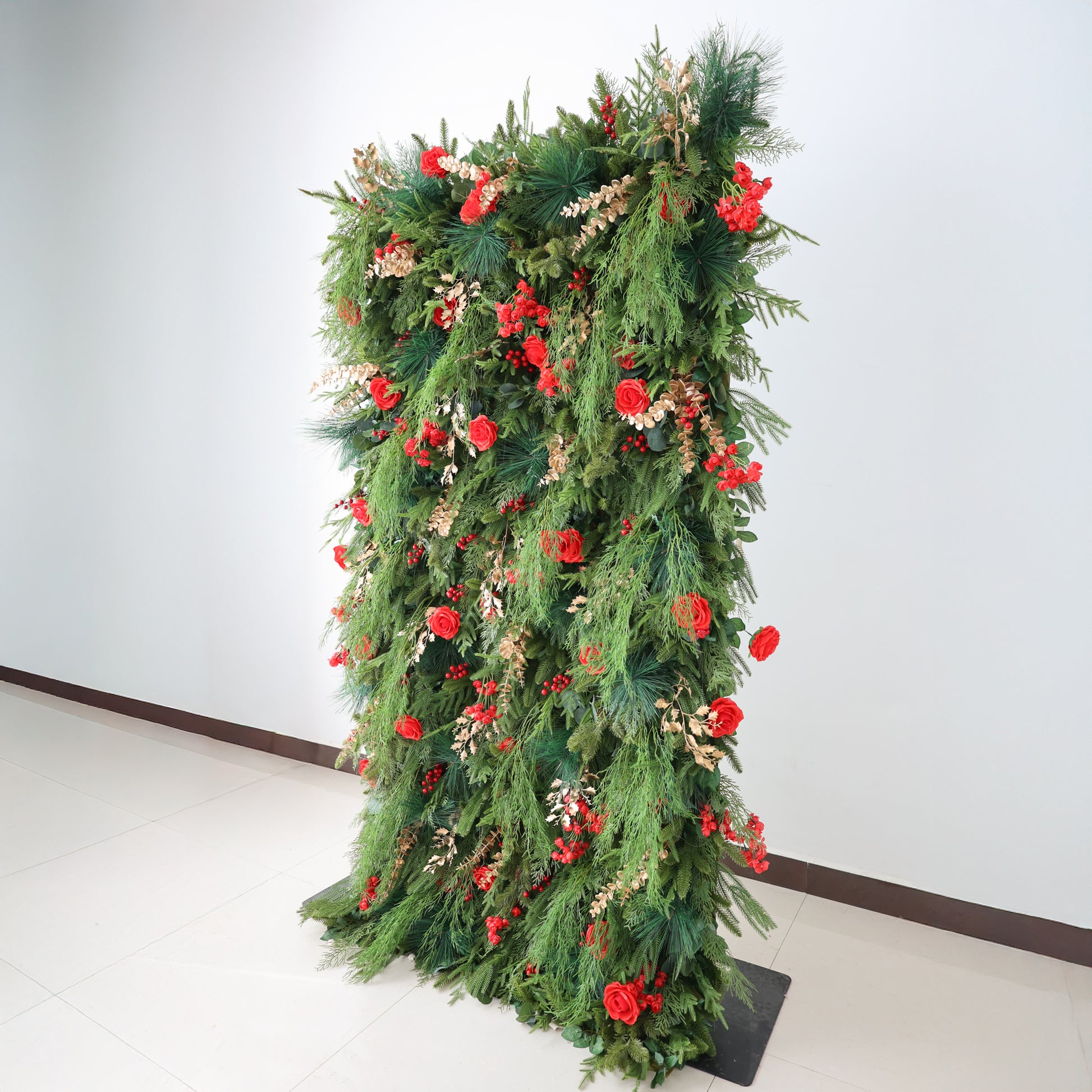 This image features a tall, lush floral installation. It's densely covered with green foliage, vibrant red roses, and clusters of red berries. Accents of golden - hued leaves add elegance. Set against a plain white wall and tiled floor, the rich, abundant arrangement exudes a warm, festive charm, ideal for decorative purposes.