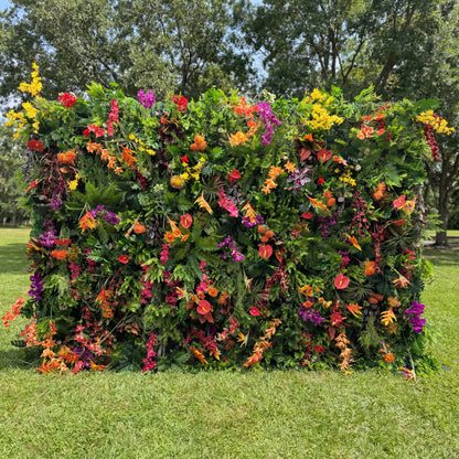 This Valar Flowers tropical flower wall backdrop is a lush, vibrant tapestry of exotic blooms and foliage, featuring fiery orange heliconias, bright red anthuriums, deep purple orchids, sunny yellow sprays, and rich green ferns. Set against a sunlit lawn, it creates a bold, jungle-inspired focal point ideal for outdoor weddings, summer parties, and lively photo opportunities, blending natural vibrancy with eye-catching color.