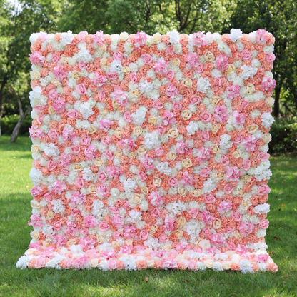 This vibrant floral wall (set on sunlit grass, tree backdrop) blends soft pinks, peachy corals, and crisp whites, layered in a dense, textured scatter of blooms. Natural light amplifies the warm, cheerful palette, enhancing the airy, playful vibe. Ideal for festive events or celebrations, it serves as an eye-catching backdrop—merging bright, inviting color with lush, romantic charm to feel both lively and elegant.