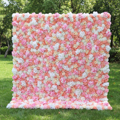 This vibrant floral wall (set on sunlit grass, tree backdrop) blends soft pinks, peachy corals, and crisp whites, layered in a dense, textured scatter of blooms. Natural light amplifies the warm, cheerful palette, enhancing the airy, playful vibe. Ideal for festive events or celebrations, it serves as an eye-catching backdrop—merging bright, inviting color with lush, romantic charm to feel both lively and elegant.