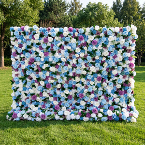 Dreamy blue artificial flower wall densely packed with sky-blue roses, creamy white blooms, vivid purple pom-pom flowers and subtle green foliage, set on a bright sunlit lawn with tall green trees. This reusable, low-upkeep floral backdrop delivers cool whimsical tones, ideal for baby boy showers, gender reveal parties, wedding photo booths and blue-themed social media shoots for refreshing, eye-catching celebration decor.