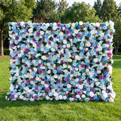 Dreamy blue artificial flower wall densely packed with sky-blue roses, creamy white blooms, vivid purple pom-pom flowers and subtle green foliage, set on a bright sunlit lawn with tall green trees. This reusable, low-upkeep floral backdrop delivers cool whimsical tones, ideal for baby boy showers, gender reveal parties, wedding photo booths and blue-themed social media shoots for refreshing, eye-catching celebration decor.