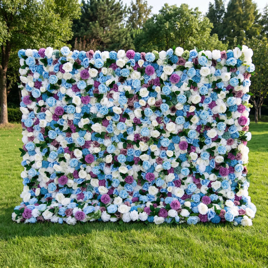 Dreamy blue artificial flower wall densely packed with sky-blue roses, creamy white blooms, vivid purple pom-pom flowers and subtle green foliage, set on a bright sunlit lawn with tall green trees. This reusable, low-upkeep floral backdrop delivers cool whimsical tones, ideal for baby boy showers, gender reveal parties, wedding photo booths and blue-themed social media shoots for refreshing, eye-catching celebration decor.