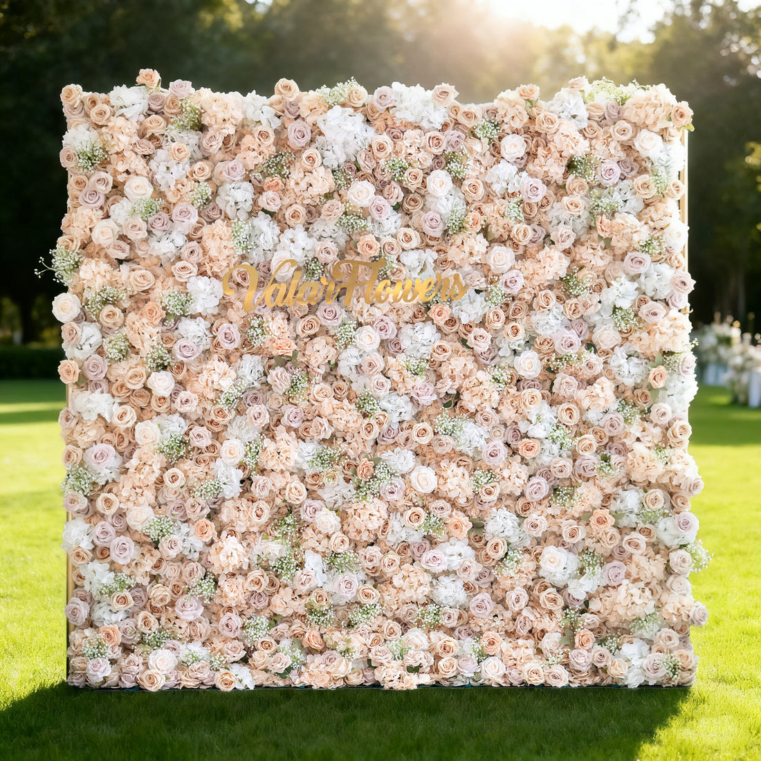This image showcases a large floral wall with a beautiful blend of soft - hued flowers, including shades of peach, cream, and white. &quot;Valar Flowers&quot; is displayed in golden text. Set outdoors on a lush green lawn under a bright sky with sunlight casting a warm glow, it creates an elegant and romantic atmosphere, perfect for events or decorative displays, exuding a sense of natural beauty and refinement.