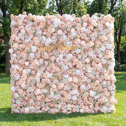 This outdoor backdrop (set on lush green grass, tree-framed) is a soft, dense wall of blush, ivory, and pale pink blooms—roses, peonies, and baby’s breath—creating an airy, romantic texture. A polished, cursive "Valar Flowers" gold sign anchors the center, contrasting gently with the muted, elegant palette. The delicate display exudes sophistication, perfect for wedding decor, garden events, or upscale photo setups.