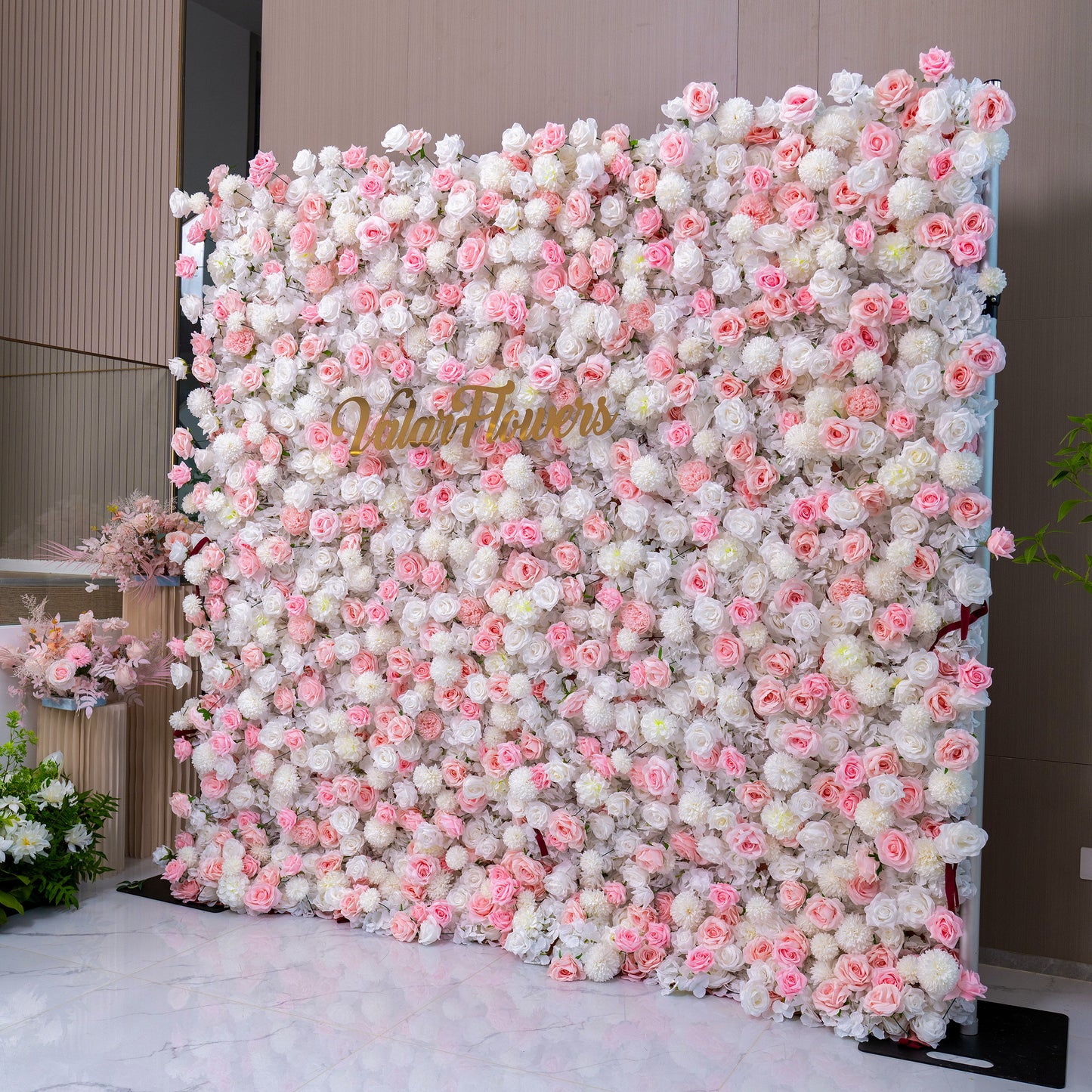 The image shows a stunning floral wall adorned with an abundance of pink and white flowers. Prominently displayed in the center is the text "Valar Flowers," suggesting it's a decorative backdrop for weddings or events.
