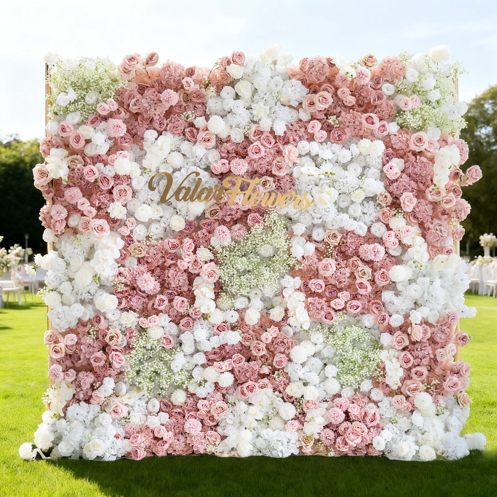 This image showcases a large floral wall with a beautiful blend of pink and white flowers, including roses and baby's breath. "Valar Flowers" is displayed in golden text. Set outdoors on a lush green lawn, with event setups like white chairs in the background under a bright sky, it creates a soft, elegant, and romantic atmosphere, perfect for occasions such as weddings or celebrations.
