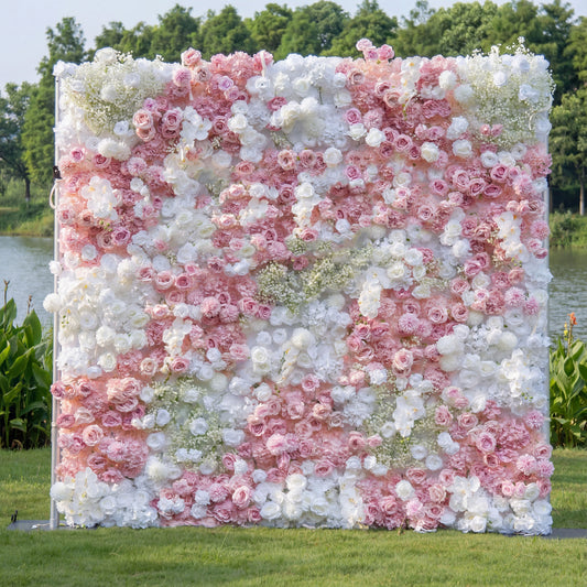A lush floral wall from Valar Flowers features a romantic palette of blush pink, creamy white, and soft peach blooms—including roses, peonies, and delicate baby's breath—arranged in a dense, textured pattern. Set against a serene lakeside backdrop, it creates a dreamy, elegant atmosphere ideal for wedding backdrops, photo booths, or special event decor.